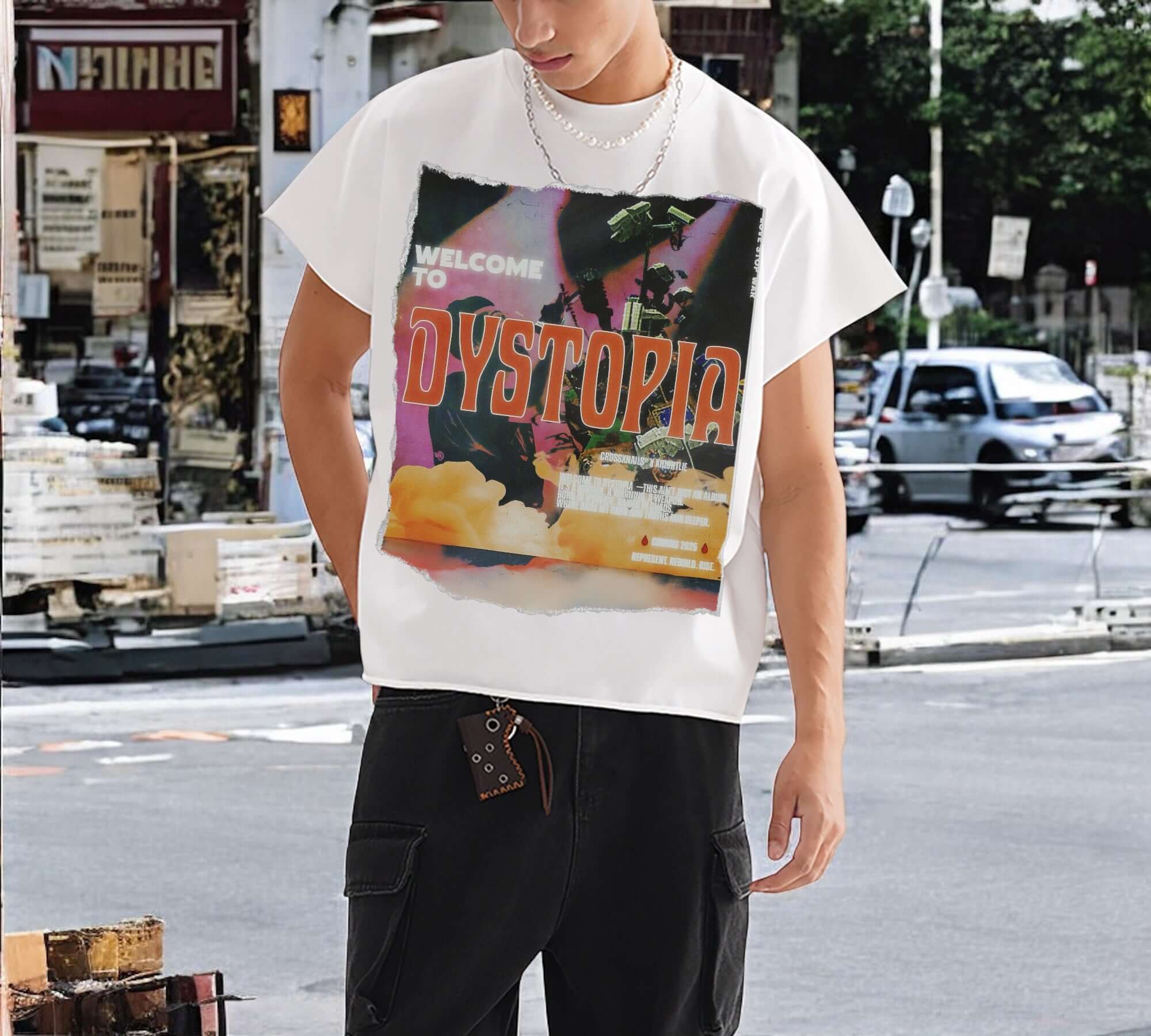 Man wearing a white oversized graphic t-shirt with ‘Dystopia’ print, paired with black cargo pants, standing on a city street — part of the Crossxnails® DYSTOPIA Collection.